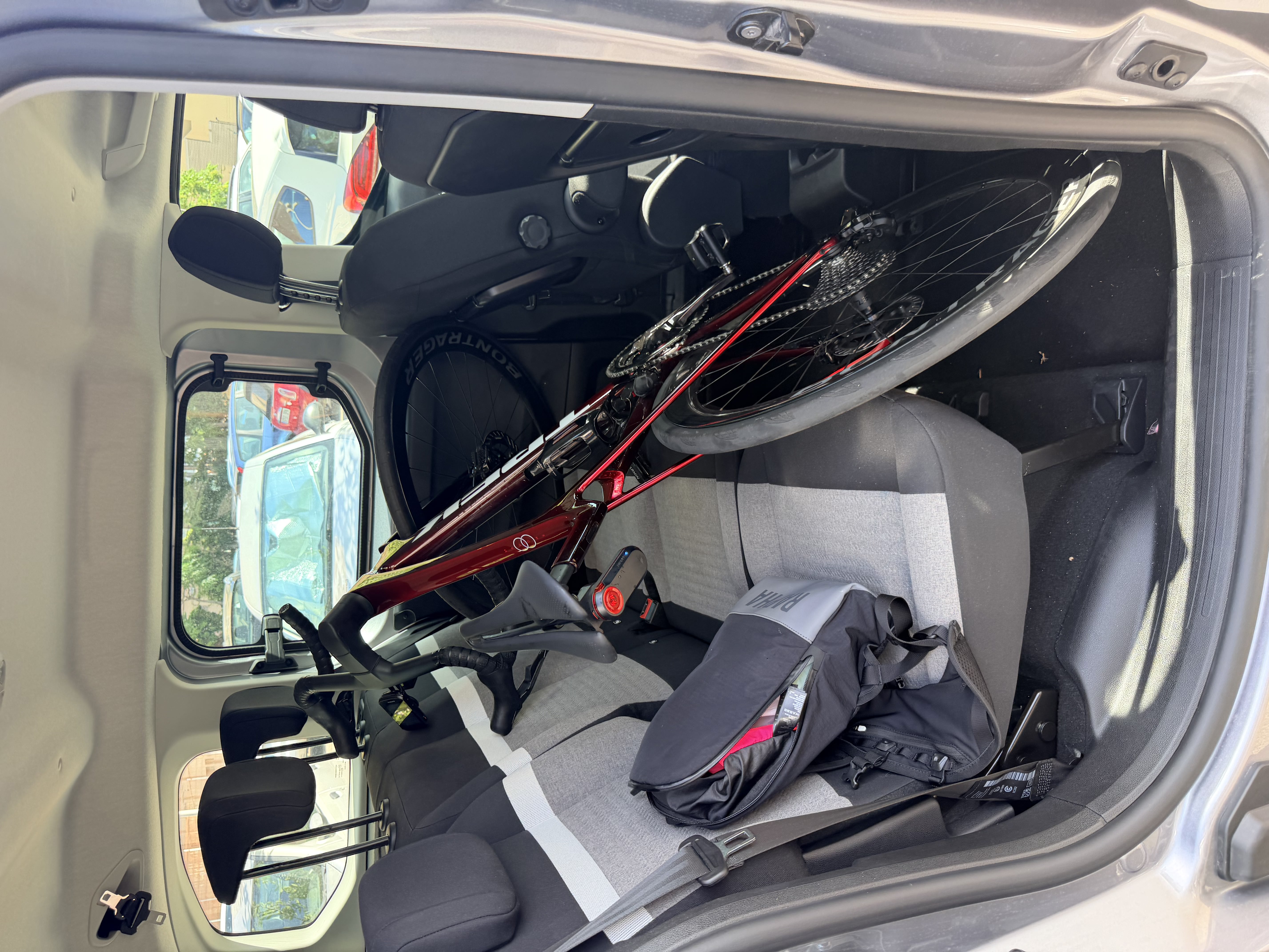 Trek Madone bike laid across rear seat of hire car with seats left upright, with Rapha bag